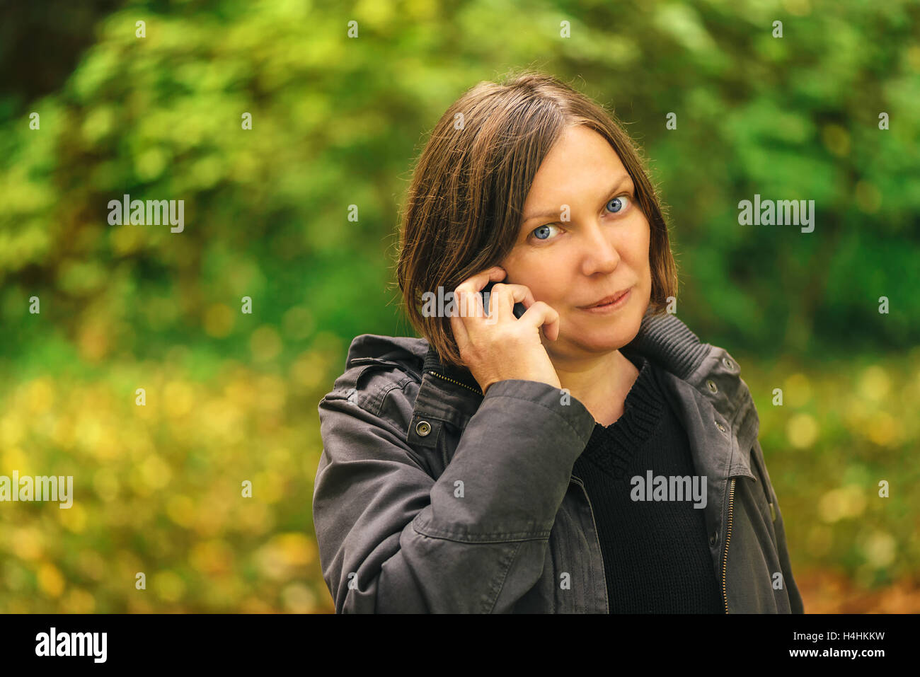 Schöne Frau am Handy im Herbst Park. Junge Erwachsene weibliche Person mit Smartphone für Unterhaltung. Stockfoto