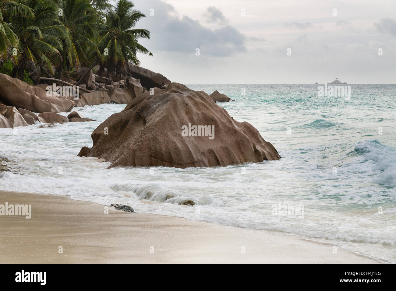 Schöner Strand Anse Patates, La Digue, Seychellen mit Granitfelsen an einem bewölkten Tag, einer kleinen Insel im Hintergrund Stockfoto