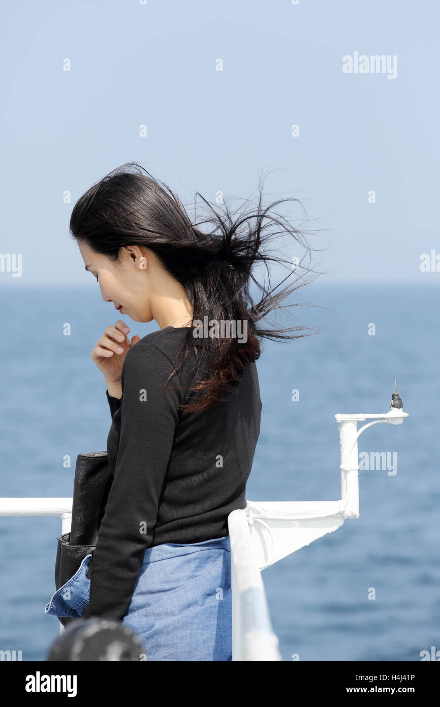 junge Asiatin mit wehenden langen Haaren mit Blick auf das Meer vom Deck des Kreuzfahrtschiffes Stockfoto