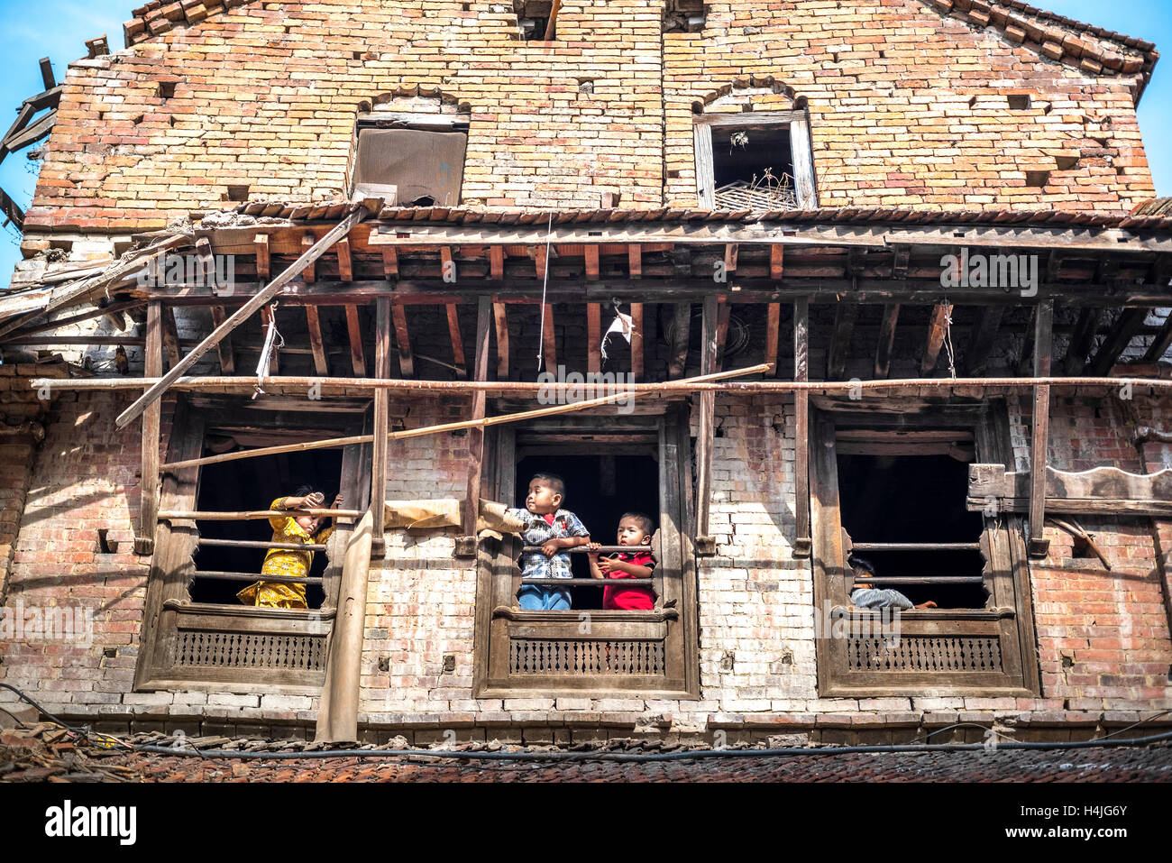 Kinder spielen an den Fenstern eines Hauses, das 2015 durch das Erdbeben in Bhaktapur, Nepal, zerstört wurde. Stockfoto