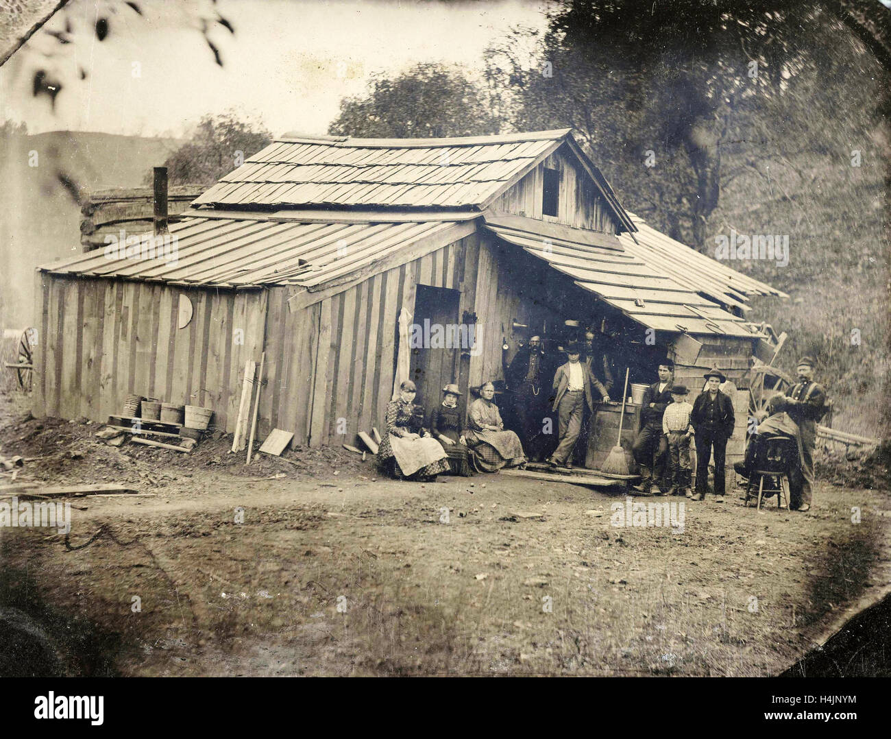 Ansicht eines Holzhauses mit zehn Leuten, von die einer schneiden und / oder rasiert, anonym, ca. 1870-1900 Stockfoto