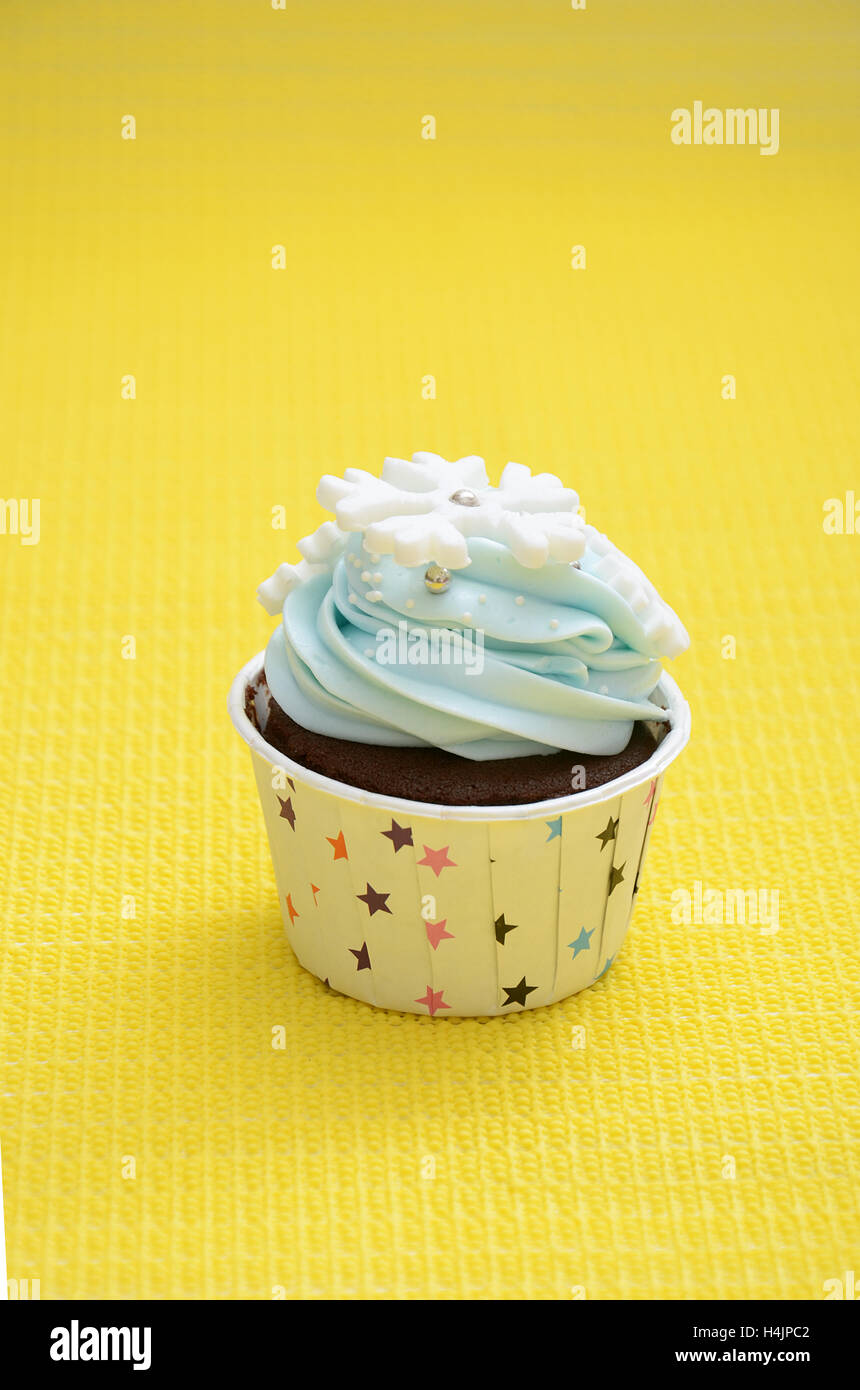 einzelne Tasse Kuchen mit Schneeflocken, die Verzierung in der Farbe hellblau für eine Geburtstagsfeier mit gelbem Hintergrund Stockfoto