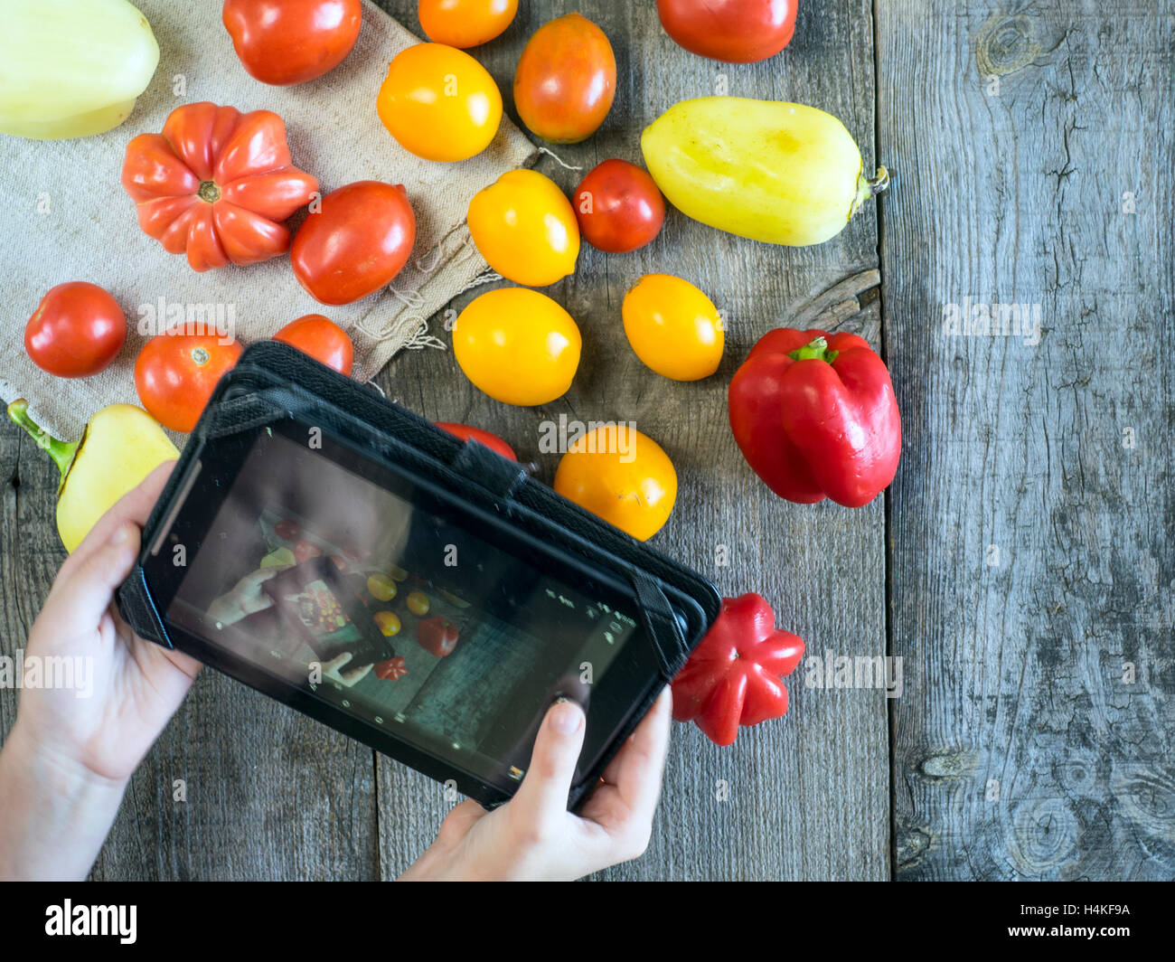 Junge in Tablet reflektiert, wenn He schießen saftige Tomaten, Glocke und Chilischote auf dem Holztisch-Ansicht Top Stockfoto
