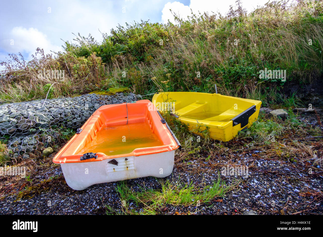 Zwei bunte Orange und gelb, die kleinen Boote auf einem Stein Ufer mit Regenwasser gefüllt Stockfoto