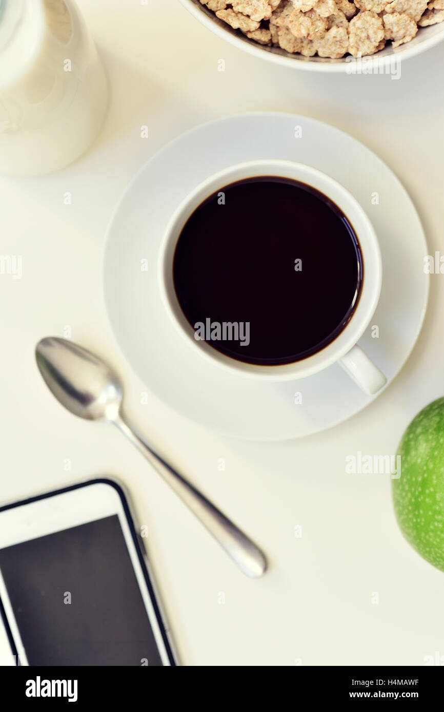 High-Angle Shot von einem weißen Tisch legen Sie zum Frühstück mit einem grünen Apfel, eine Tasse Kaffee und eine Schüssel mit Müsli und ein smartphone Stockfoto