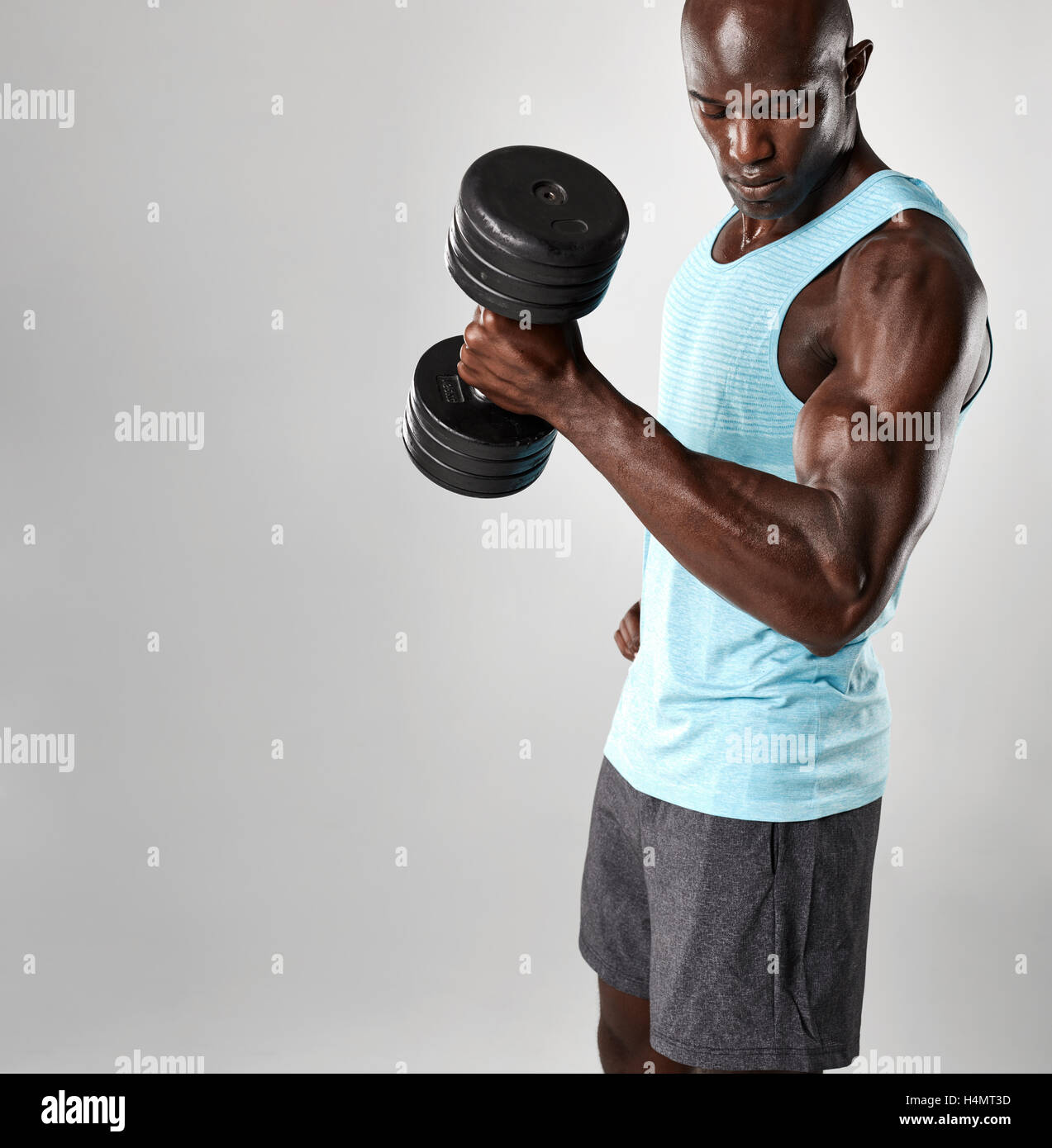 Passen Sie junge Afrikaner trainieren mit Hanteln vor grauem Hintergrund. Muskulöse Schwarze Männermodel heben schwerere Hanteln. Stockfoto