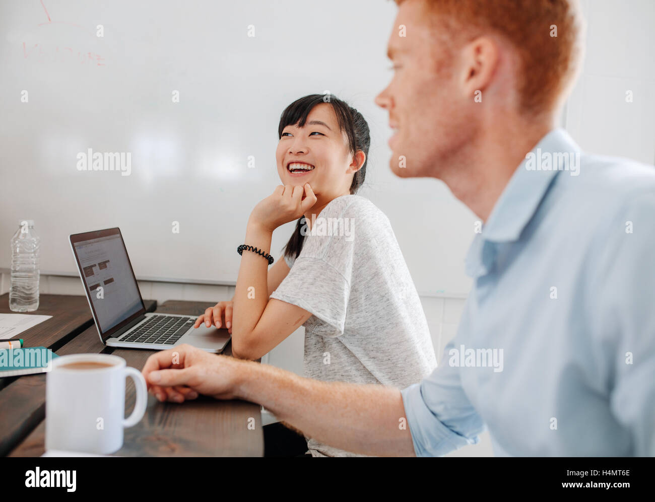 Zwei glückliche junge Geschäftsleute beim Business-Meeting am Konferenztisch sitzen. Mitarbeiter im Sitzungssaal mit Laptop sitzen Stockfoto