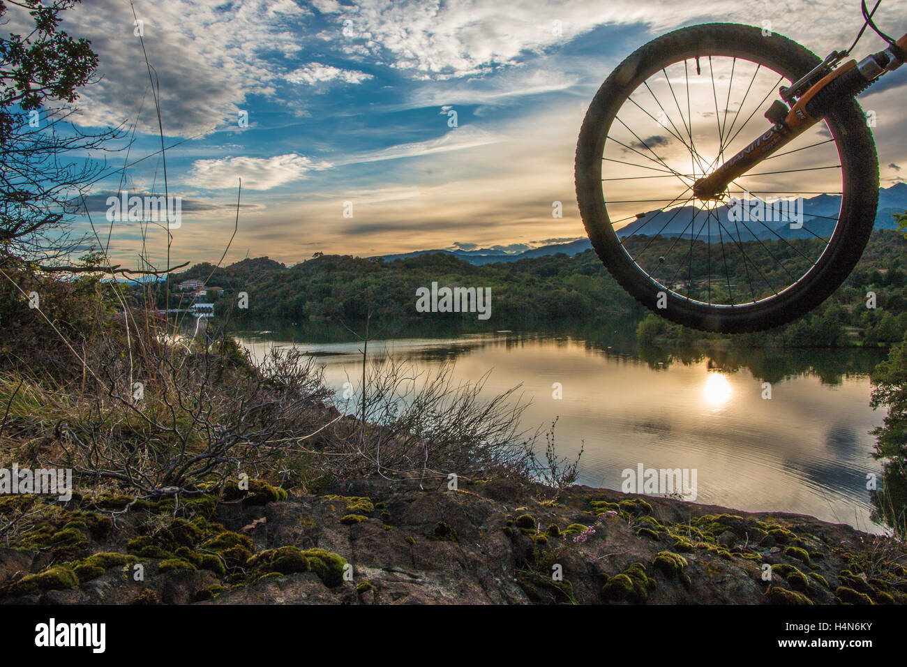 Ein Mountainbike-Fahrrad-Rad bei Sonnenuntergang mit der Spiegelung der Sonne im See Stockfoto