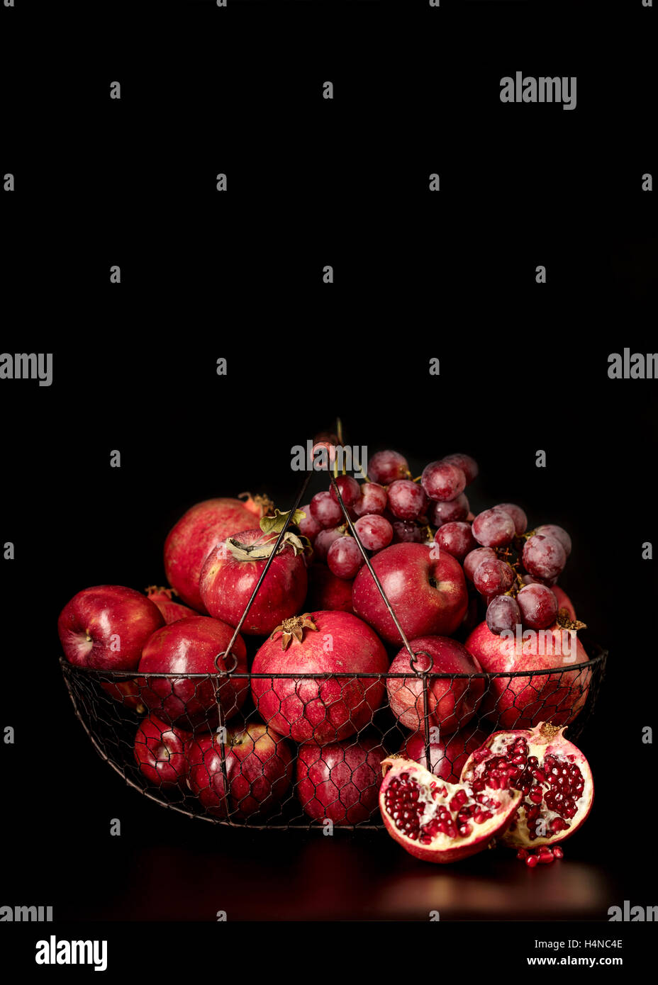 Still-Leben auf einem dunklen Hintergrund. Früchte und Beeren (Äpfel, Granatäpfel und Trauben) in den Korb. Stockfoto