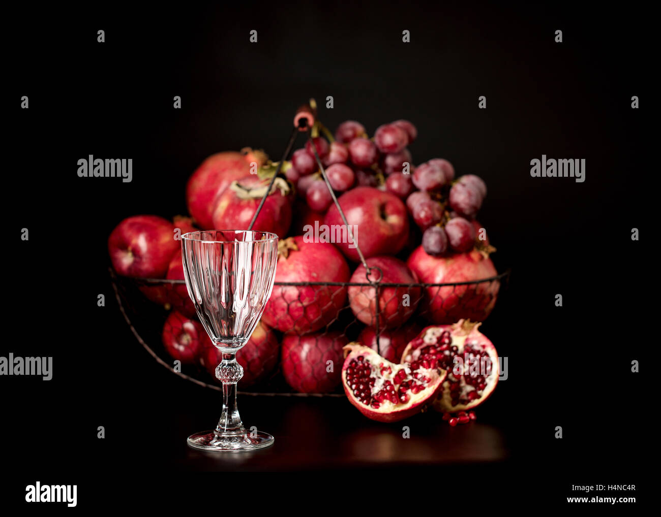 Still-Leben auf einem dunklen Hintergrund. Weingläser (Liquor), Früchte und Beeren (Äpfel, Granatäpfel und Trauben) in den Korb. Stockfoto