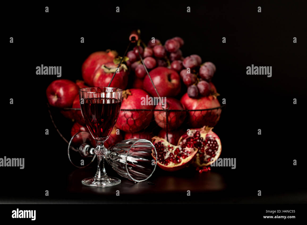 Still-Leben auf einem dunklen Hintergrund. Weingläser (Liquor), Früchte und Beeren (Äpfel, Granatäpfel und Trauben) in den Korb. Stockfoto