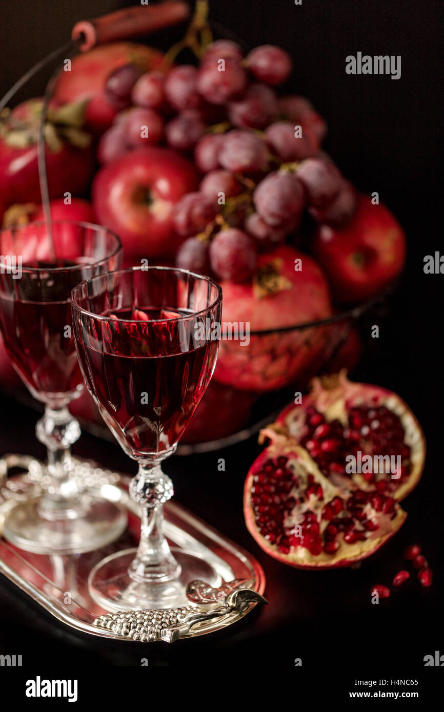 Still-Leben auf einem dunklen Hintergrund. Weingläser (Liquor), Früchte und Beeren (Äpfel, Granatäpfel und Trauben) in den Korb. Stockfoto