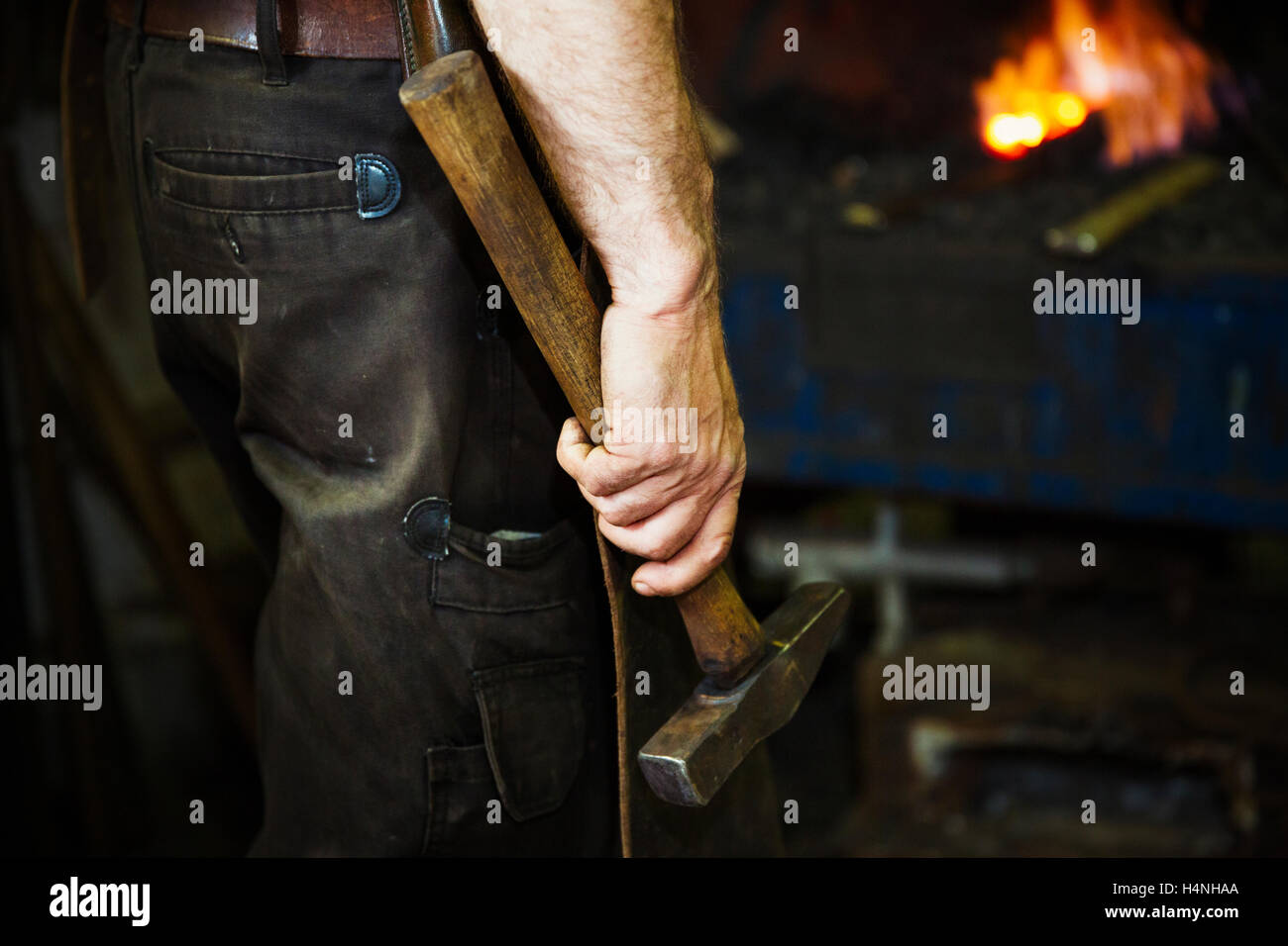 Ein Mann in eine Lederschürze hält einen Hammer in einer Werkstatt. Stockfoto