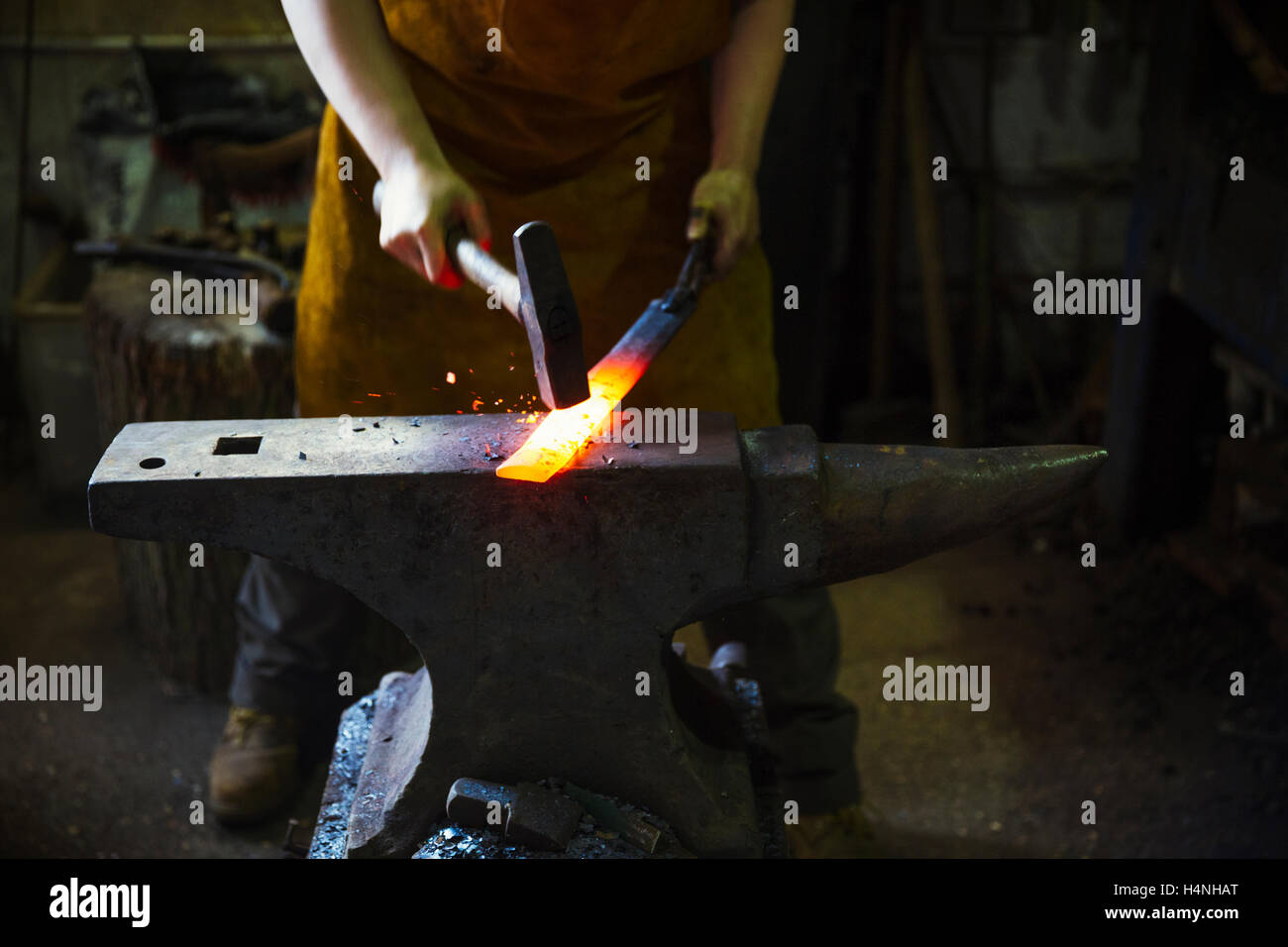 Ein Schmied schlägt eine Länge von roten Roheisen am Amboss mit einem Hammer in eine Werkstatt. Stockfoto