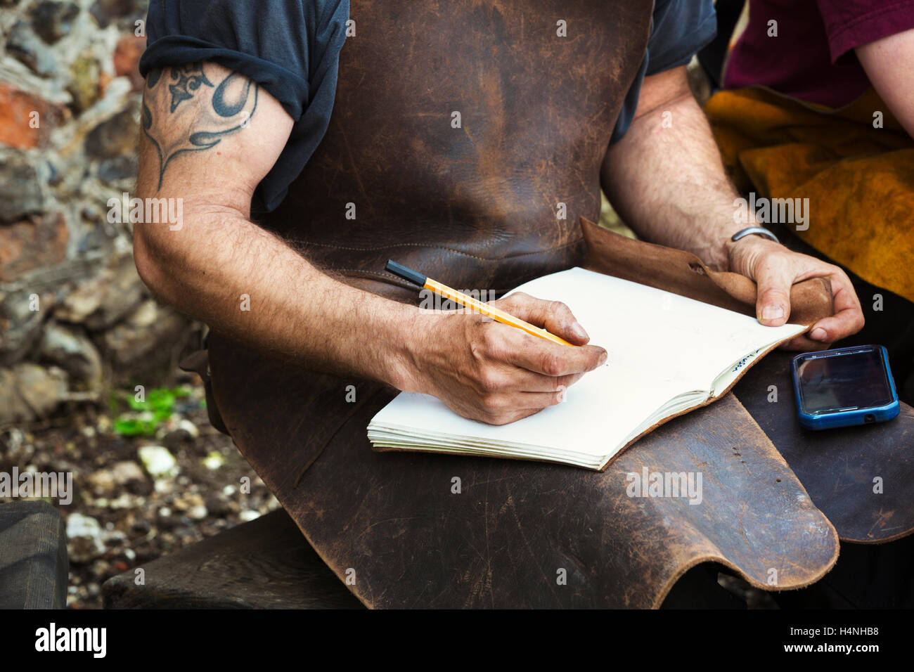 Zwei Menschen, Mann und Frau Schmiede tragen Lederschürzen in ein Notizbuch schreiben saß in einem Garten. Stockfoto