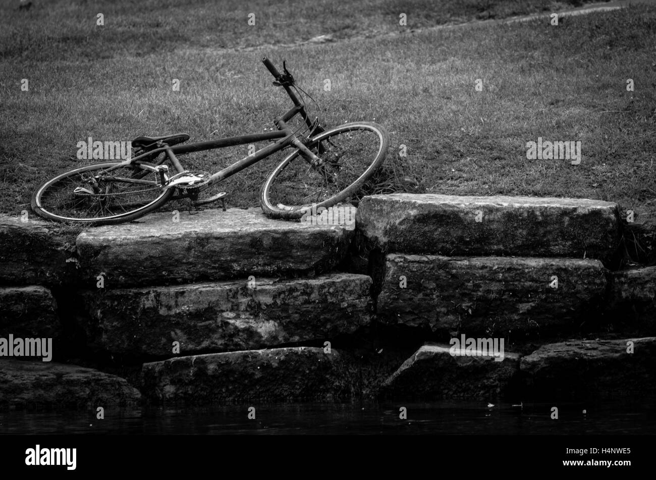 altes Fahrrad auf Stein Wand und Grass Rande des Flusses aufgegeben Stockfoto