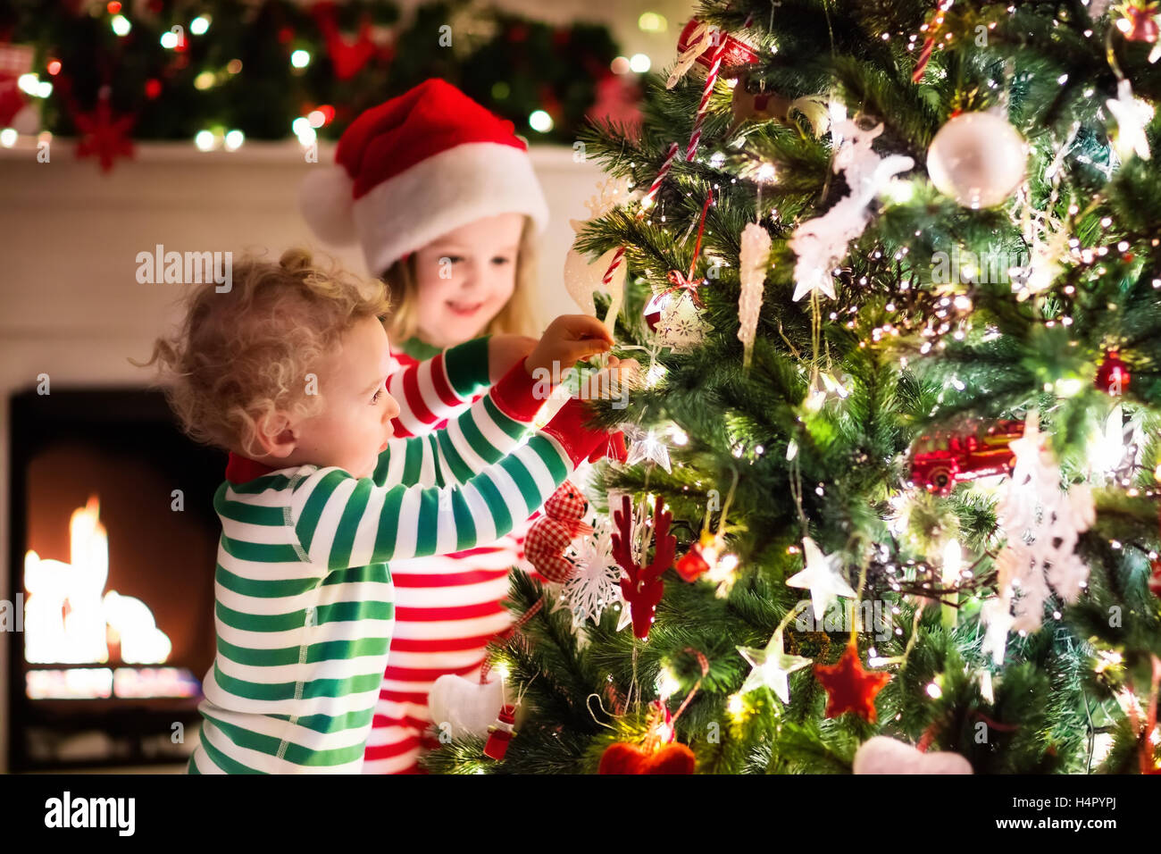 Glückliche kleine Kinder die passenden rot und grün gestreiften Pyjama dekorieren Weihnachtsbaum im schönen Wohnzimmer mit Kamin. Stockfoto