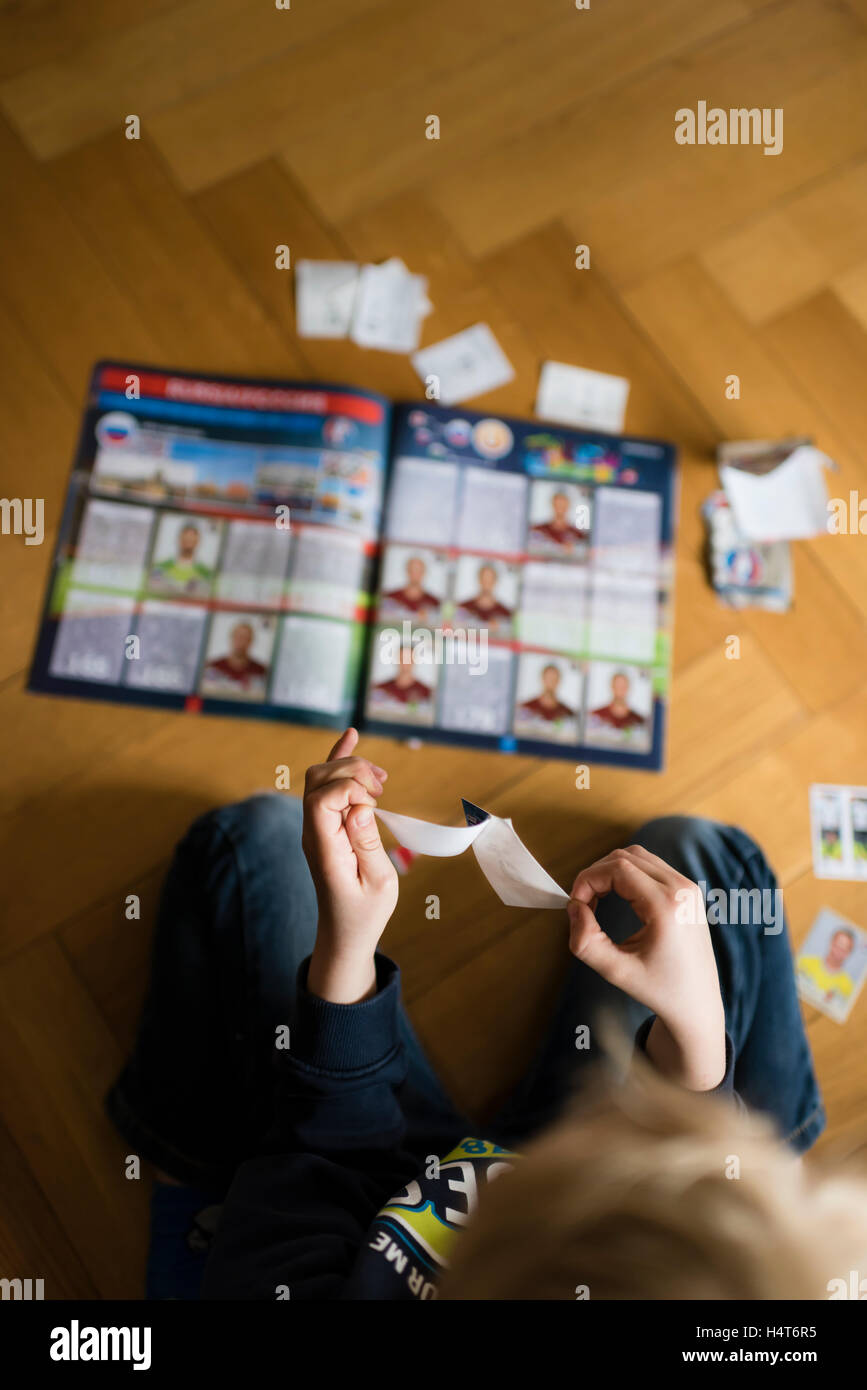 Ein 8 Jahre alter Junge ist Fußball-Sammelkarten in seinem Aufkleber Sammlung Sammelalbum einfügen. Stockfoto