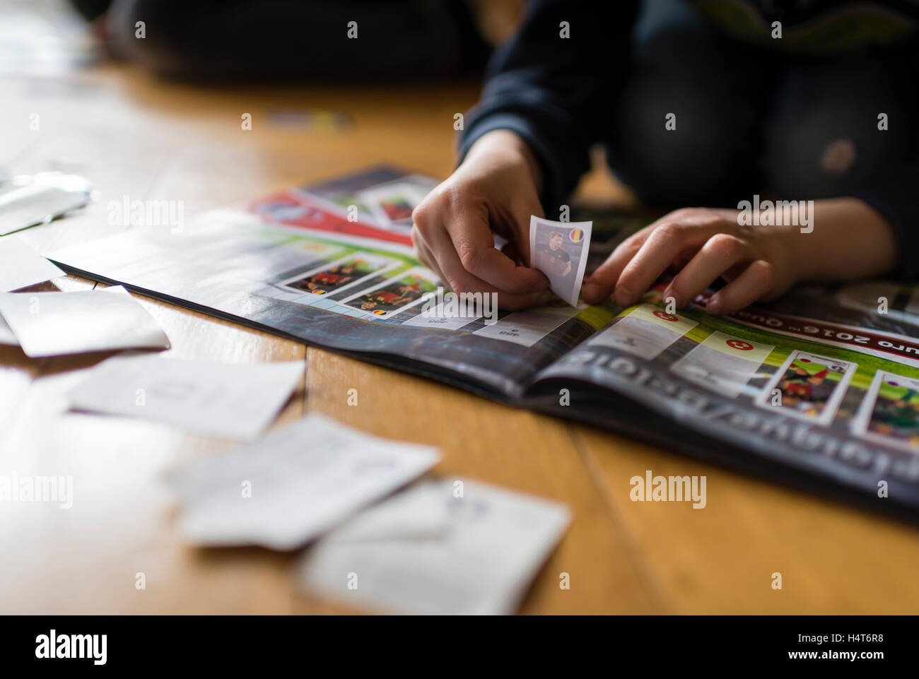 Ein 8 Jahre alter Junge ist Fußball-Sammelkarten in seinem Aufkleber Sammlung Sammelalbum einfügen. Stockfoto