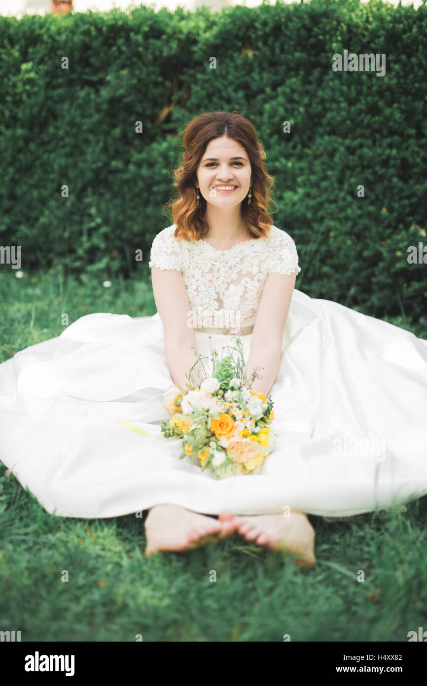 Schöne Braut sitzt am Boden halten einen Blumenstrauß in die Kamera Lächeln Stockfoto