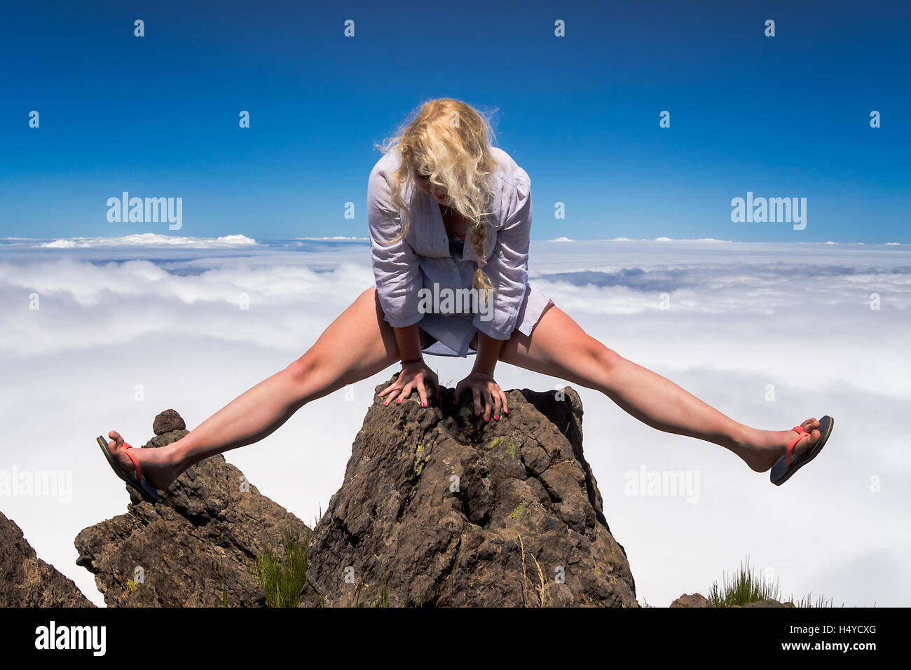 Junge blonde Frau Acrobat machen spaltet sich auf Felsen am Gipfel des Berges. Stockfoto