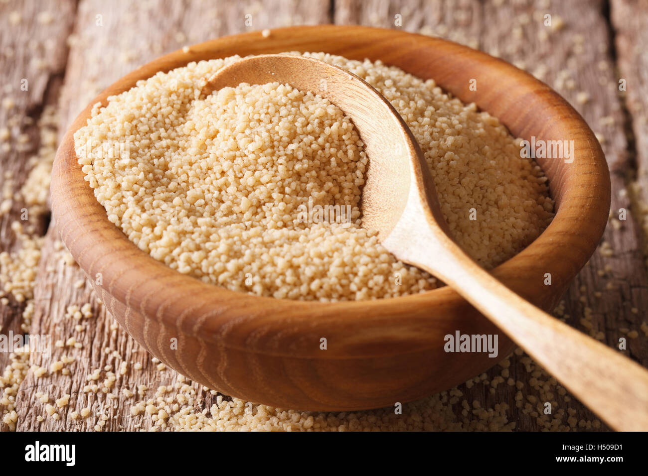 Den trockenen Couscous in einer Holzschale mit einer Nahaufnahme der Löffel auf dem Tisch. horizontale Stockfoto