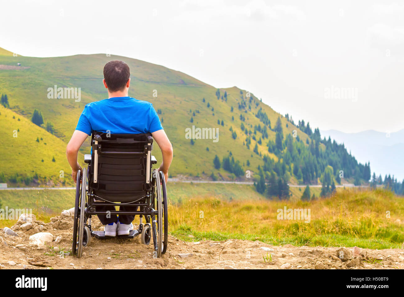 Junger Mann im Rollstuhl an der frischen Luft an einem sonnigen Tag auf dem Berg Stockfoto