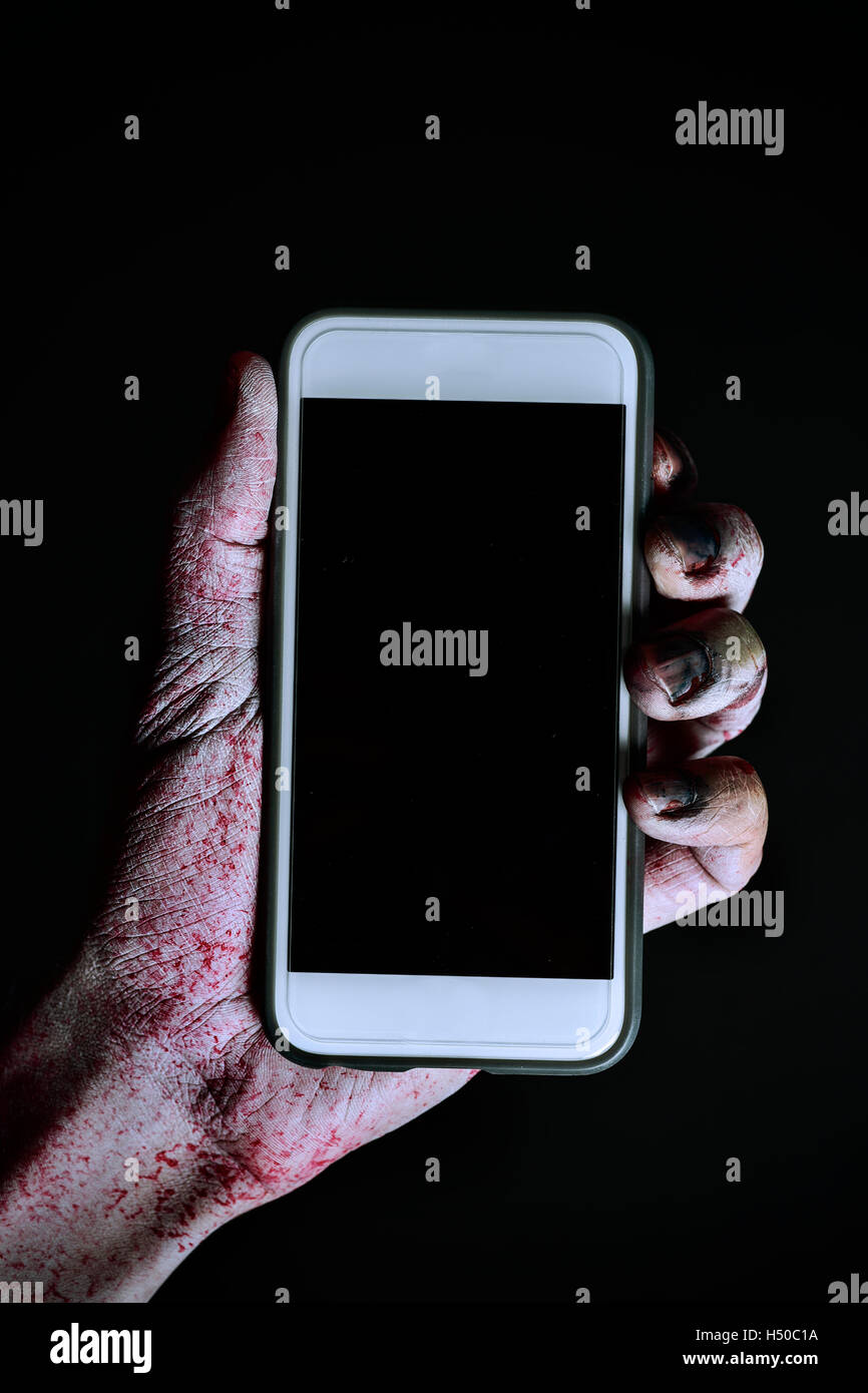 Nahaufnahme von einer unheimlich und blutige Hand hält eine Smartphone mit schwarzen Leerzeichen in seinem Bildschirm vor einem schwarzen Hintergrund Stockfoto