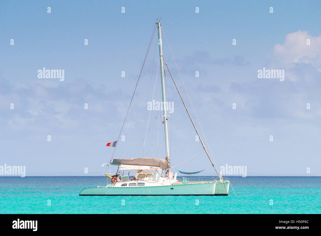 Katamaran mit französischer Flagge verankert in einem türkisfarbenen karibischen Meer. Stockfoto