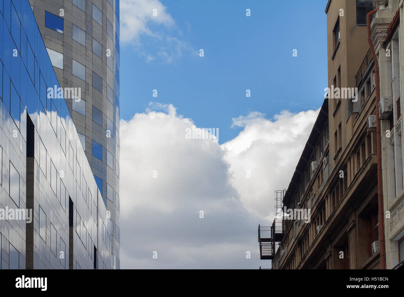 Side-by-Seite Foto von klassischen Gebäude vor moderne gläserne Bürogebäude mit blauem Himmel dazwischen Stockfoto