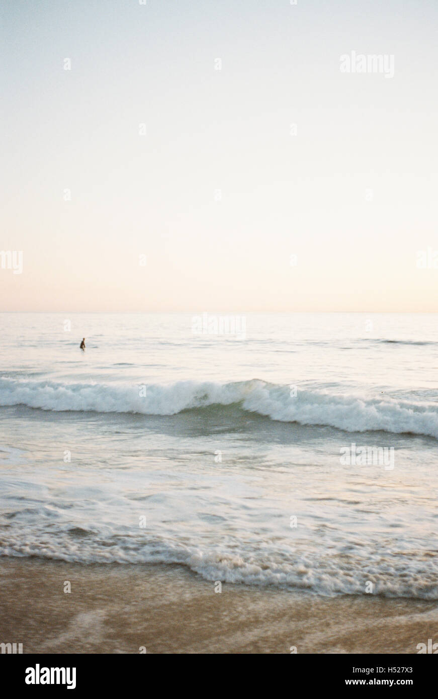 Ozean-Welle rollt auf einen Sandstrand, Person im Hintergrund. Stockfoto