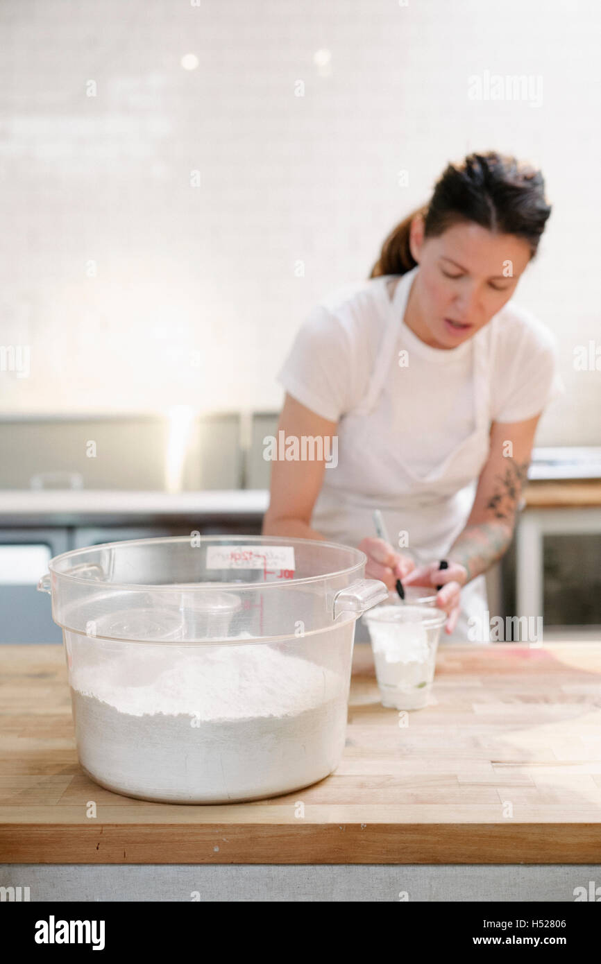 Frau trägt eine weiße Schürze an einem Schalter der Arbeit in einer Bäckerei Mehl zu messen. Stockfoto