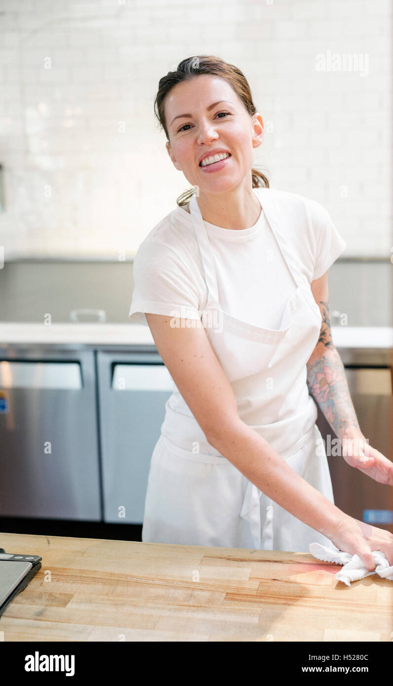 Frau trägt eine weiße Schürze an einem Schalter der Arbeit in einer Bäckerei mit einem Tuch abwischen. Stockfoto
