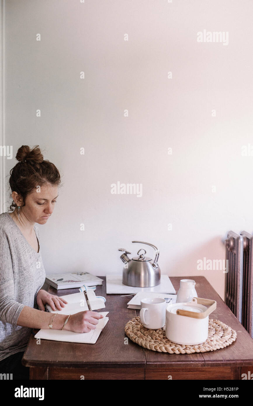 Frau sitzt an einem Tisch in ihrer Wohnung in ein Tagebuch, morgendlichen Routine zu schreiben. Stockfoto