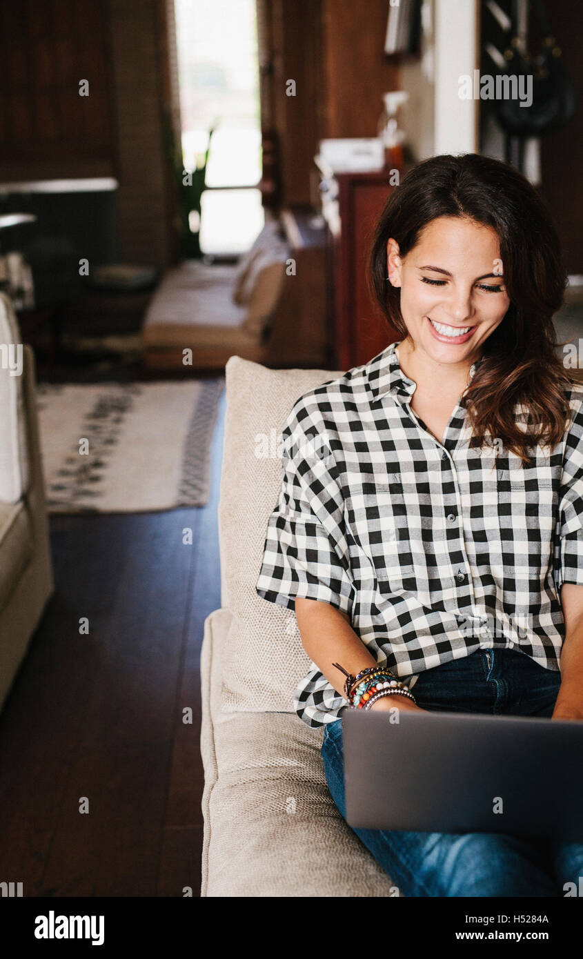 Frau mit langen braunen Haaren auf einem Sofa liegend mit einem Laptopcomputer. Stockfoto