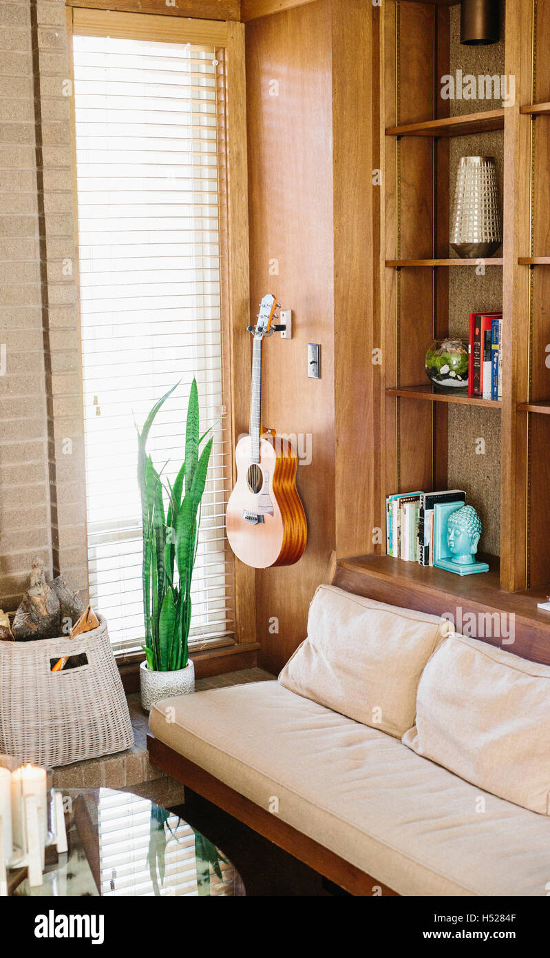 Innenansicht aus einem Wohnzimmer mit Sofa, Couchtisch, Bücherregal und Akustikgitarre an eine Wand hängen. Stockfoto