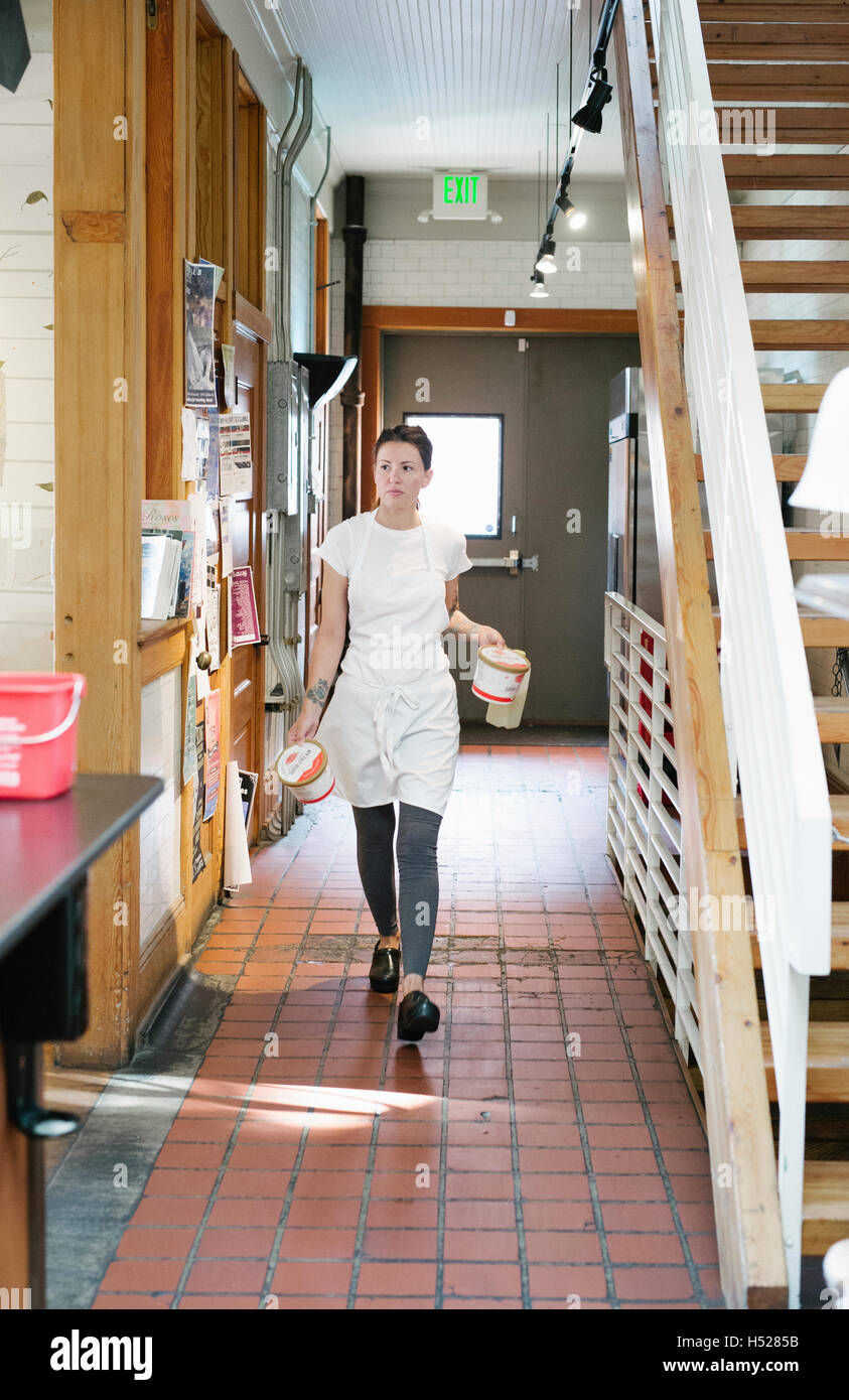 Frau trägt einen Korridor entlang Schürze tragen zwei Lebensmittel-Container. Stockfoto