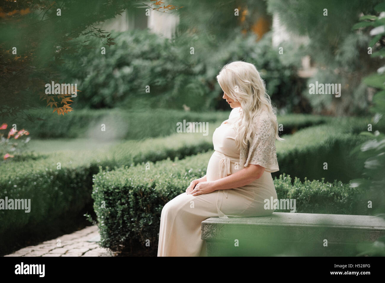 Porträt einer schwangeren Frau mit langen blonden Haaren in einem Garten. Stockfoto