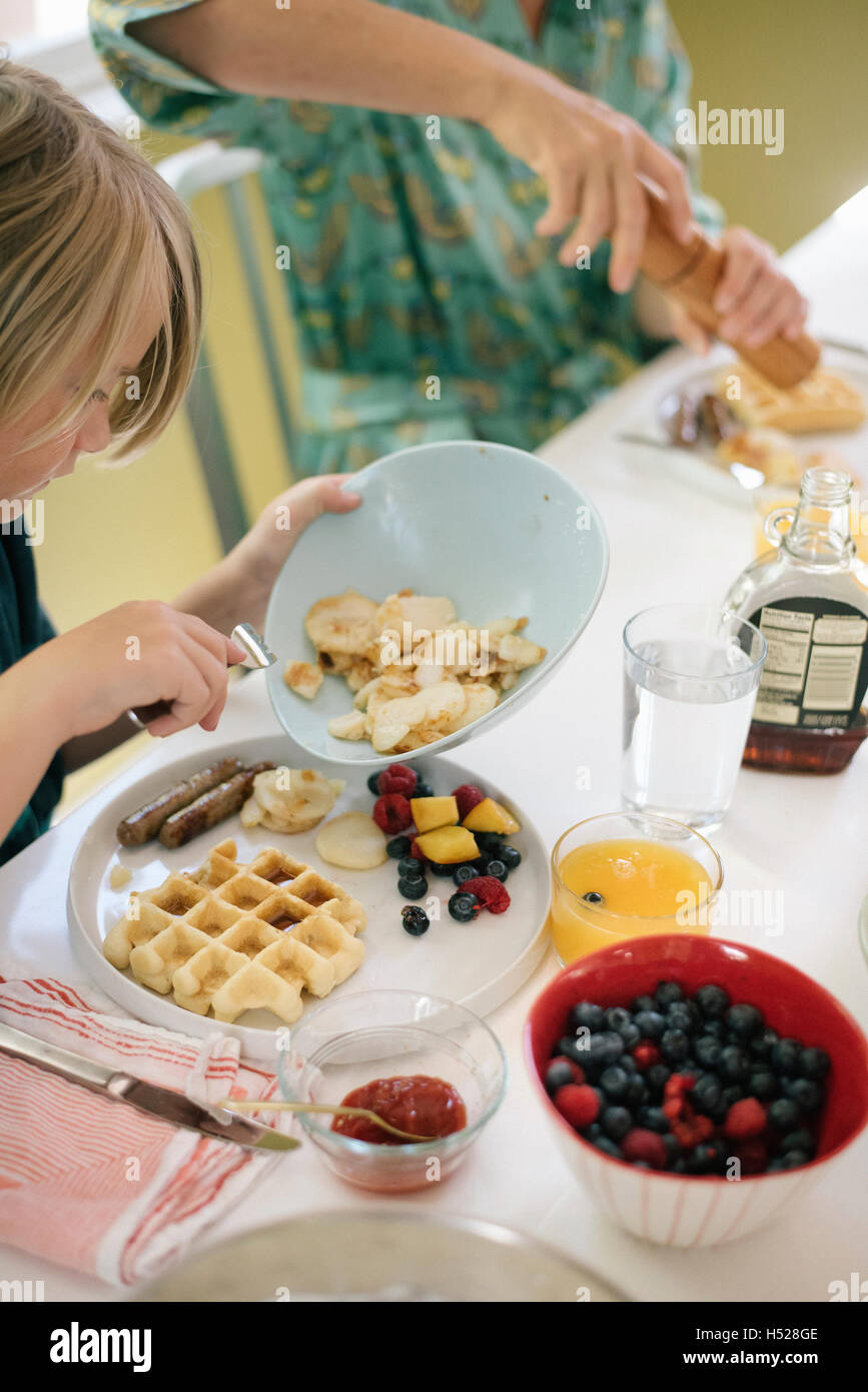 Junge sitzt am Frühstückstisch, Waffeln, Obst und Saft. Stockfoto