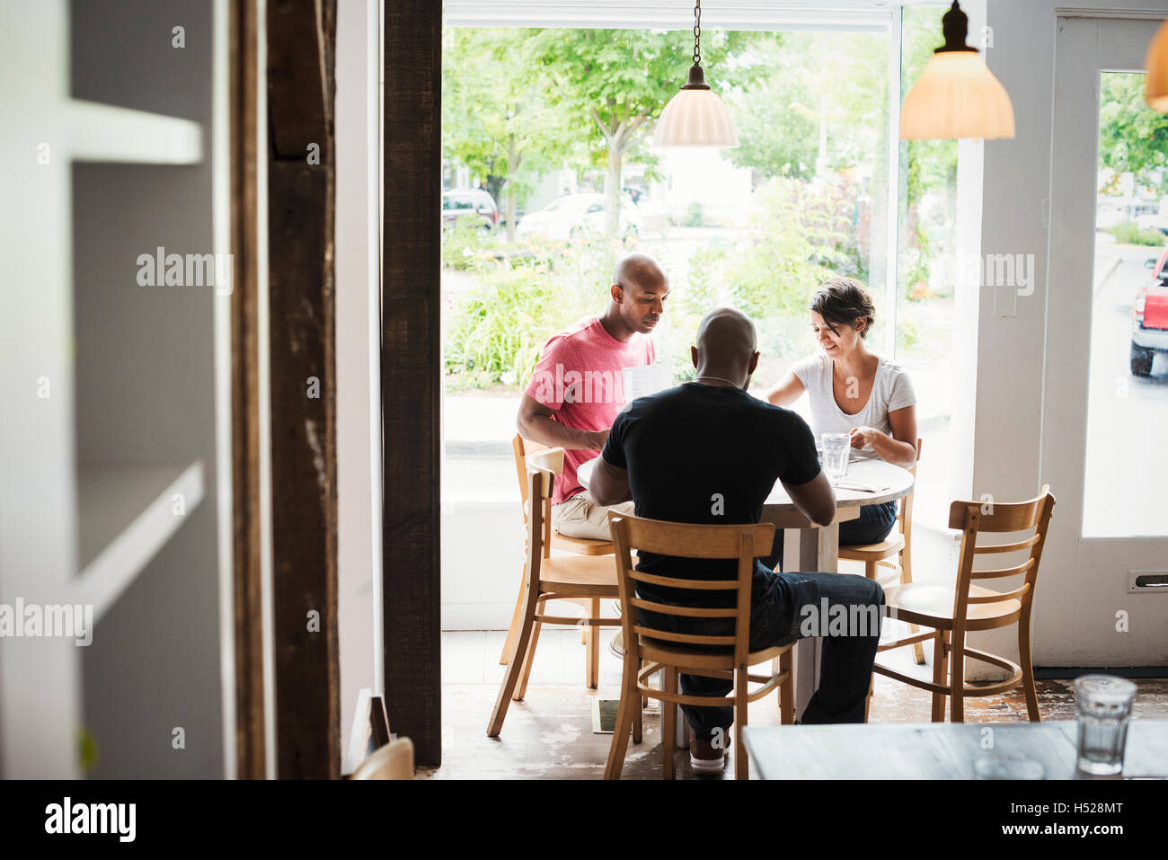 Zwei Männer und eine Frau sitzen an einem Tisch in einem Café zu Mittag. Stockfoto
