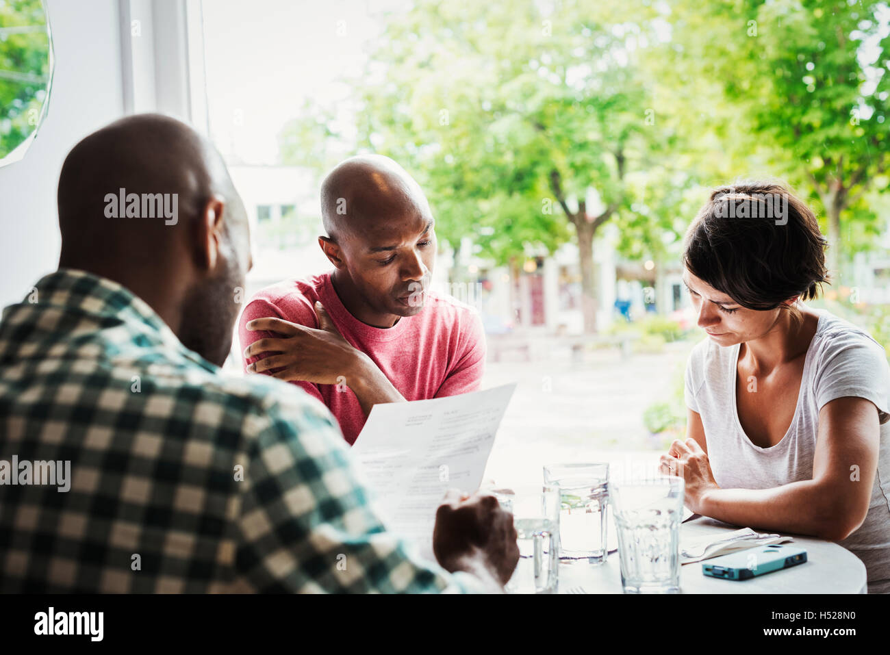 Zwei Männer und eine Frau sitzen an einem Tisch in einem Café zu Mittag. Stockfoto