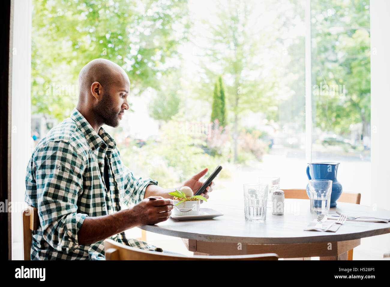 Mann trägt ein kariertes Hemd, sitzen in einem Café mit seinem Handy. Stockfoto