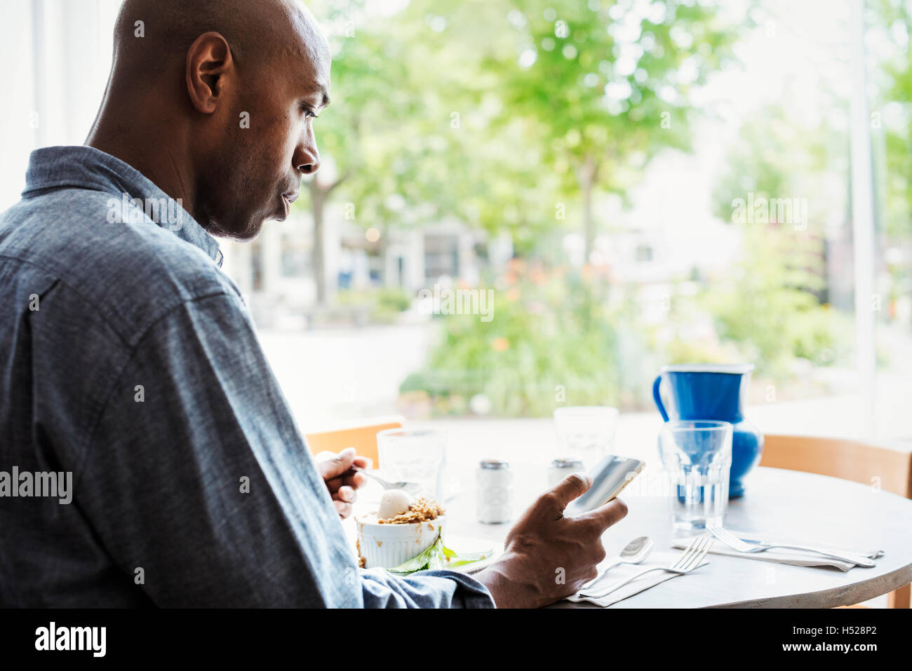 Mann trägt ein kariertes Hemd, sitzen in einem Café mit seinem Handy. Stockfoto
