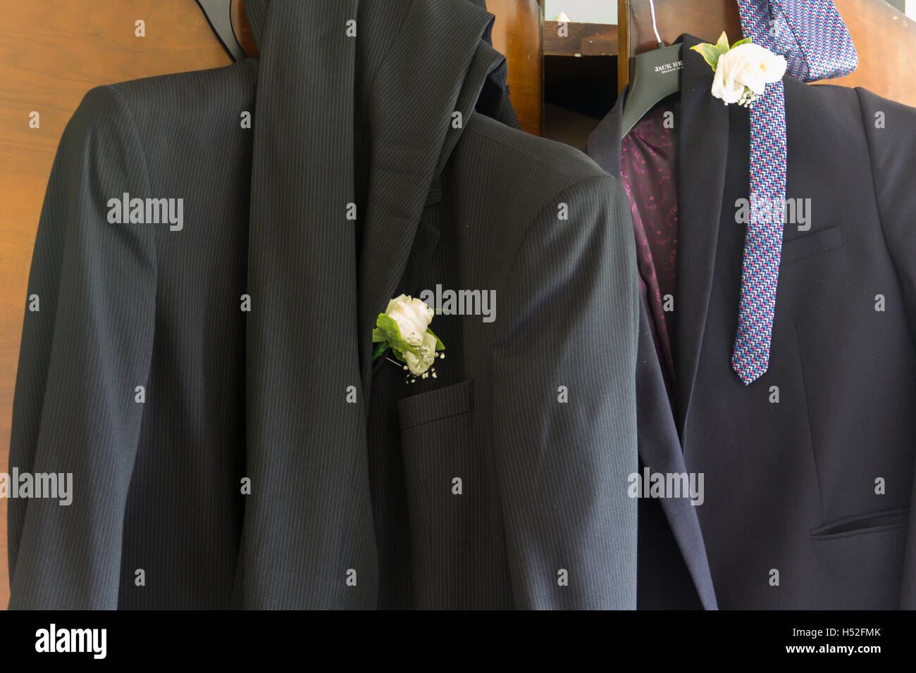 Zwei Herren Anzüge, getragen von Hochzeitsgäste, mit weißen Nelke Knopflöcher achtlos auf eine Schranktür hing nach der Veranstaltung. Stockfoto