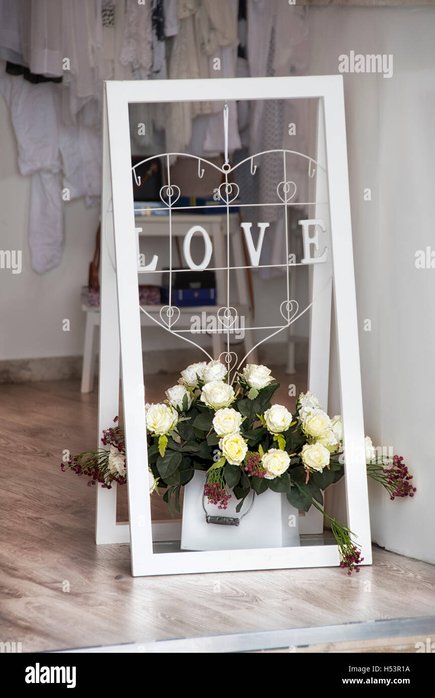 Ein weißer Rahmen mit Liebe Inschrift und weiße Rosen als Dekoration Bekleidung Shop, Boutique-Eingang Stockfoto