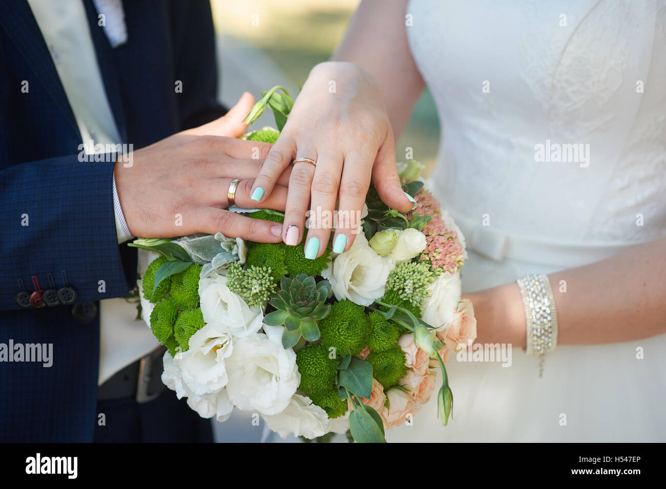 Hände von Braut und Bräutigam mit goldenen Ringen auf Hochzeit bouquet Stockfoto