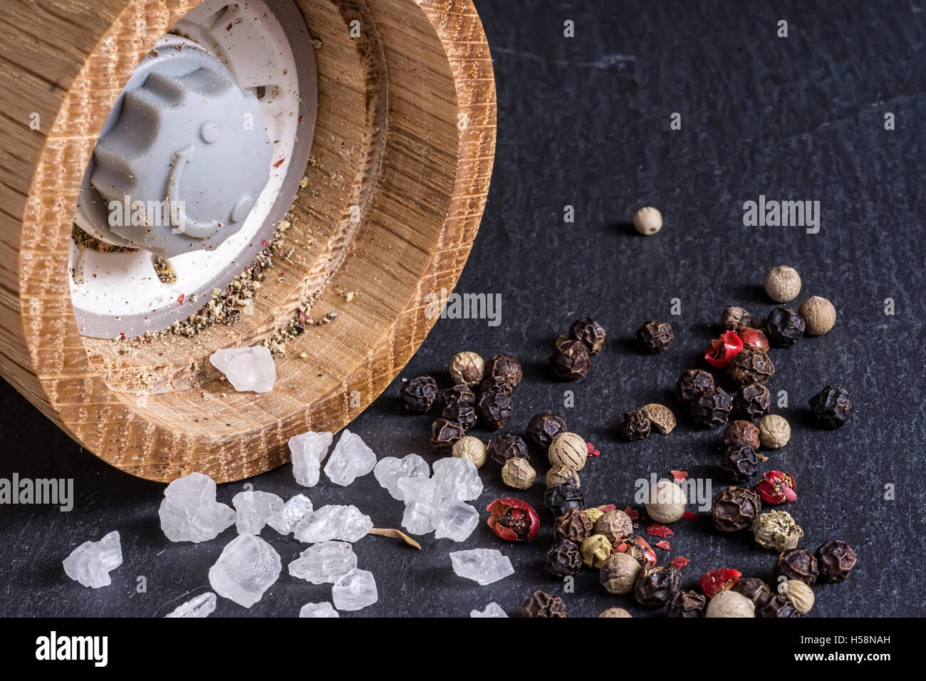 Pfeffermühle, Meersalz und Pfeffer Körner auf dunklen Steinoberfläche hautnah Stockfoto