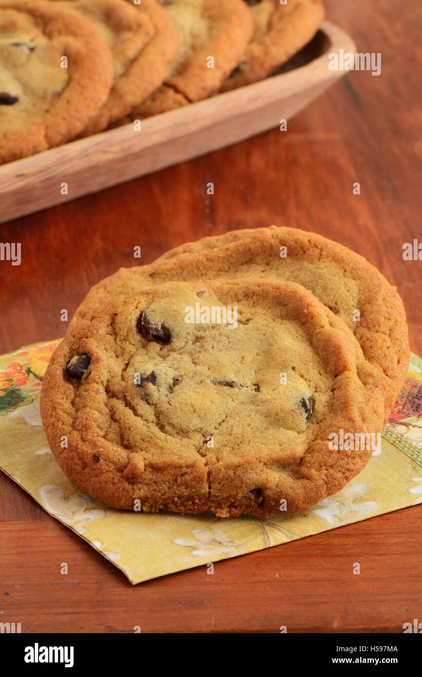Frisch gebackene Schokoladenkekse auf Serviette mit Holztablett von Cookies im Hintergrund in Hochformat.  Flachen DOF Stockfoto