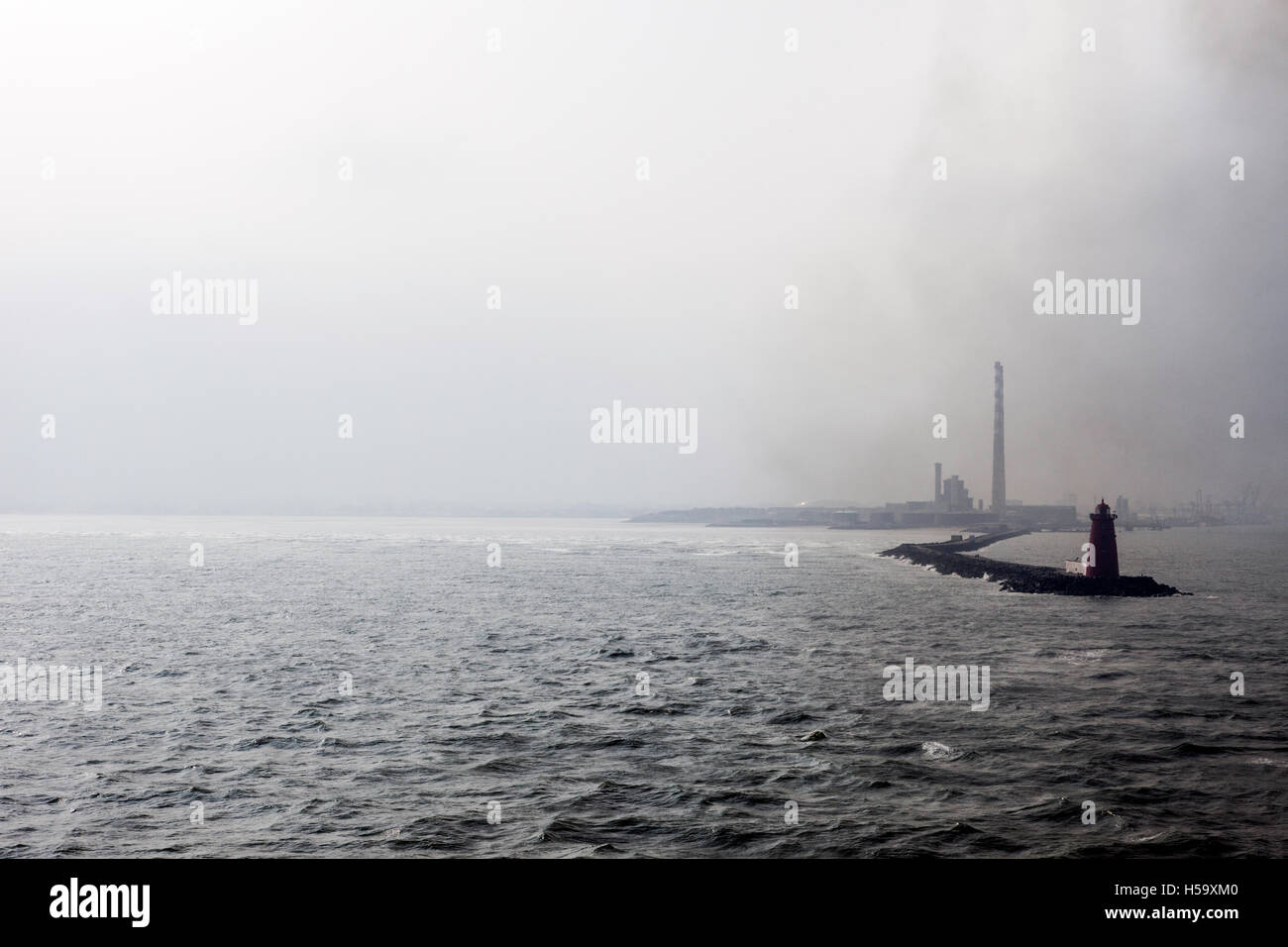 Industrielandschaft zeigt einen Leuchtturm und Rauchende Schlote, Umweltverschmutzung steigt in die Atmosphäre, Dublin, Irland. Stockfoto