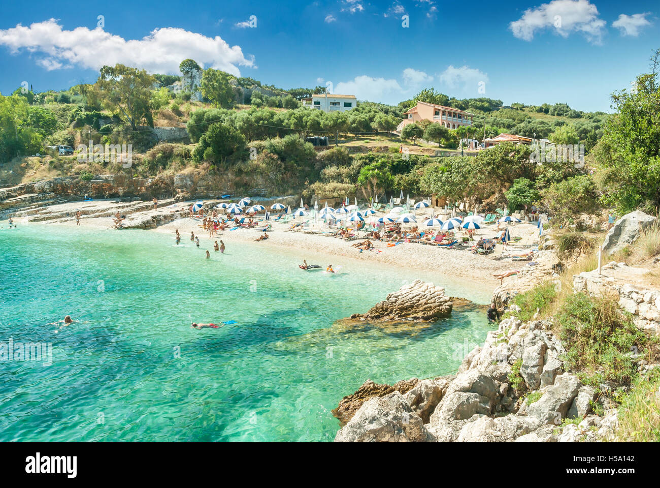 Kassiopi Beach, Korfu, Griechenland. Sonnenliegen und Sonnenschirme (Sonnenschirm) am Strand. Touristen am Strand entspannen. Stockfoto